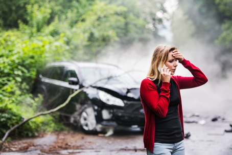 a woman on her phone standing in front of her wrecked car